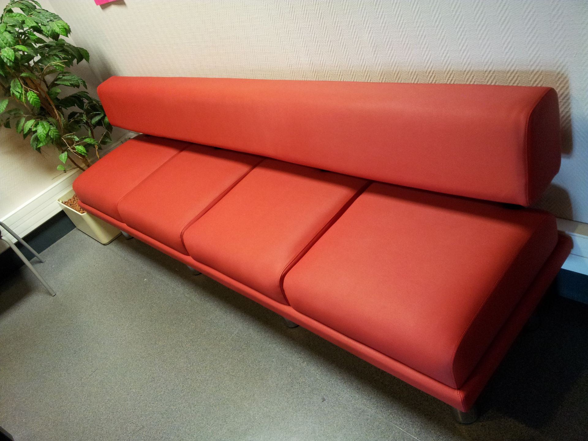 Canapé en cuir rouge contre un mur avec une plante.