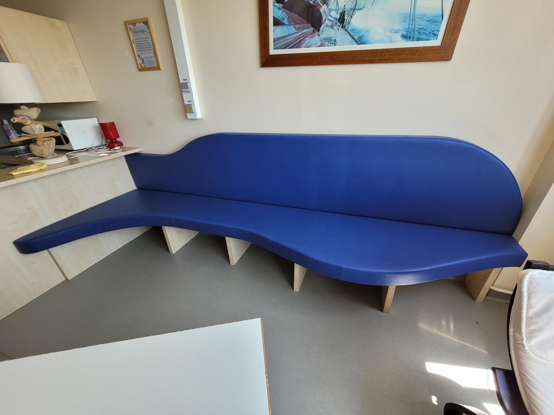Banc bleu rembourré au design ondulé et supports en bois, dans une pièce.