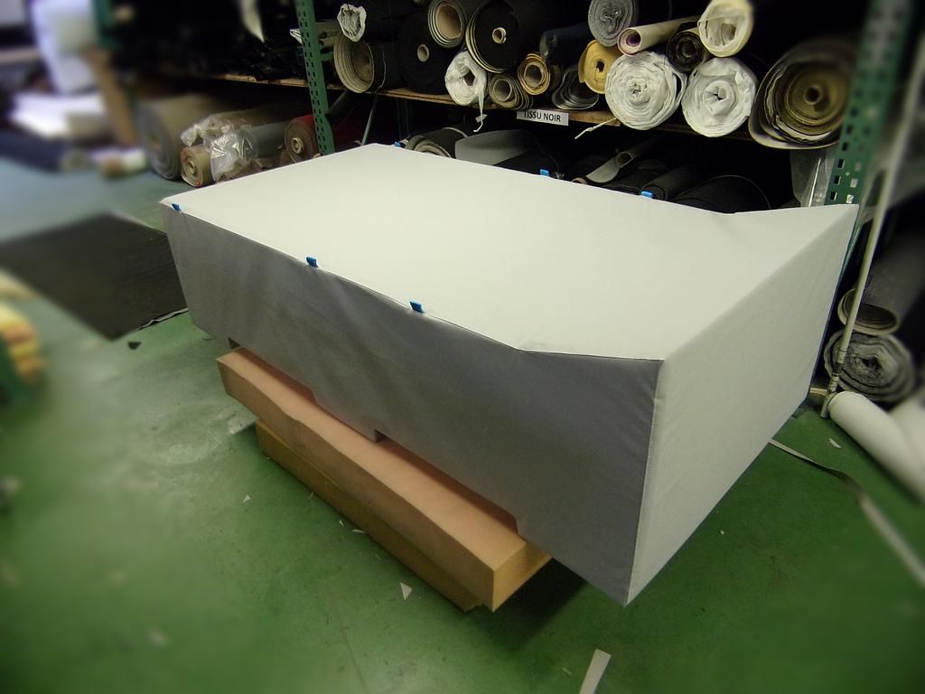 Un bloc rectangulaire enveloppé de tissu gris clair, posé sur une base en bois, dans un magasin de tissus.