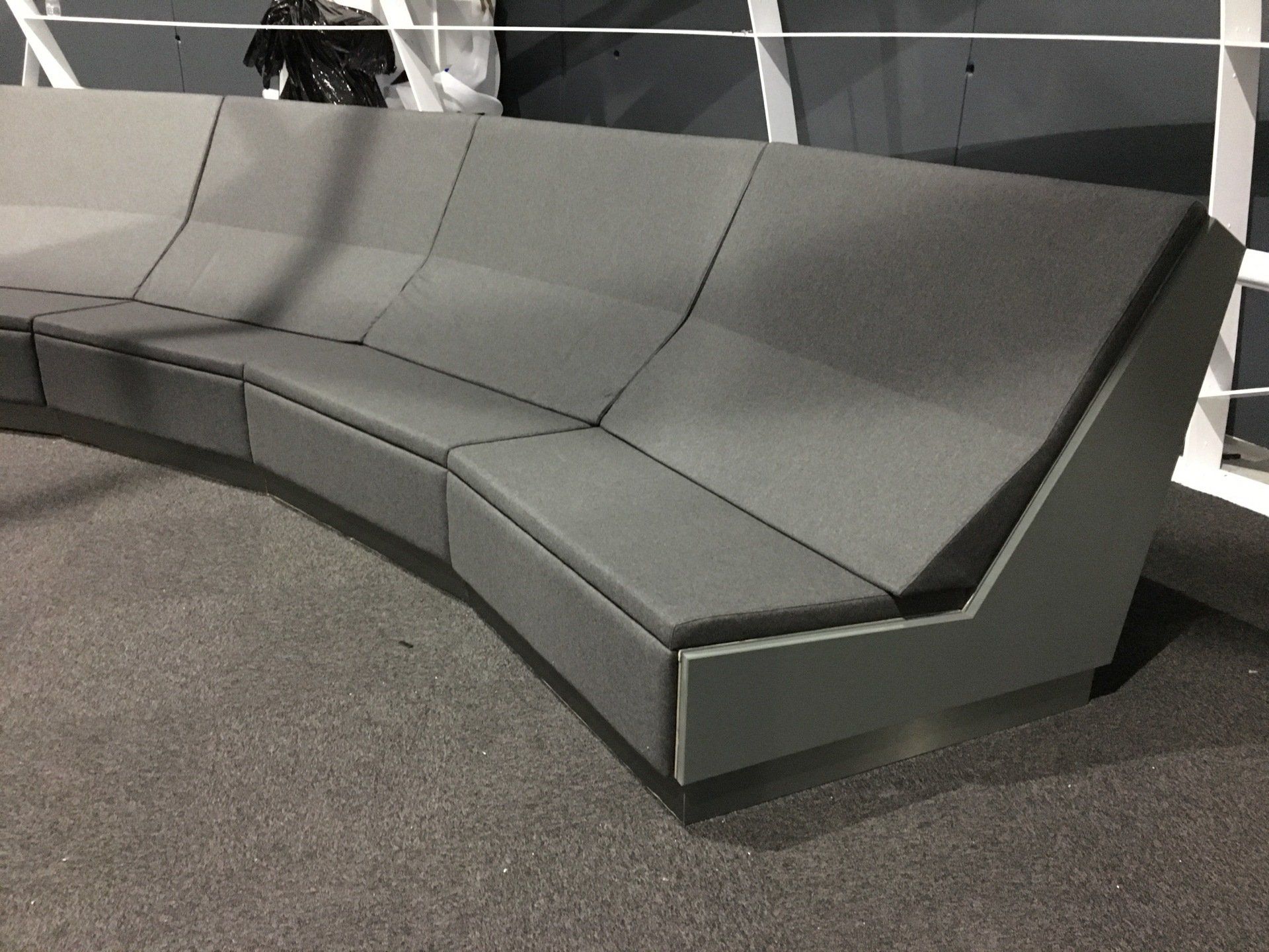 Canapé modulaire incurvé gris avec un design géométrique sur une surface recouverte de moquette grise.