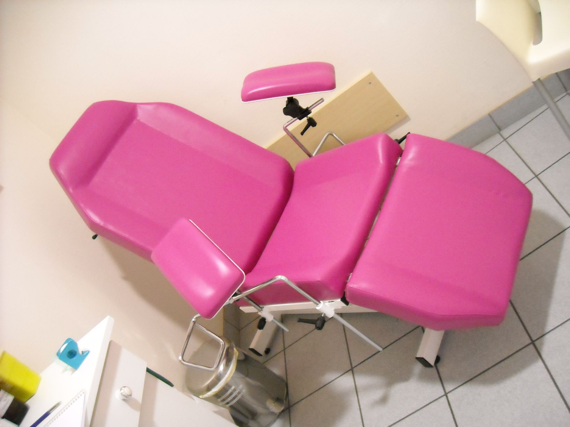 Table d'examen rose dans un cabinet médical, avec appui-tête et accoudoirs réglables.