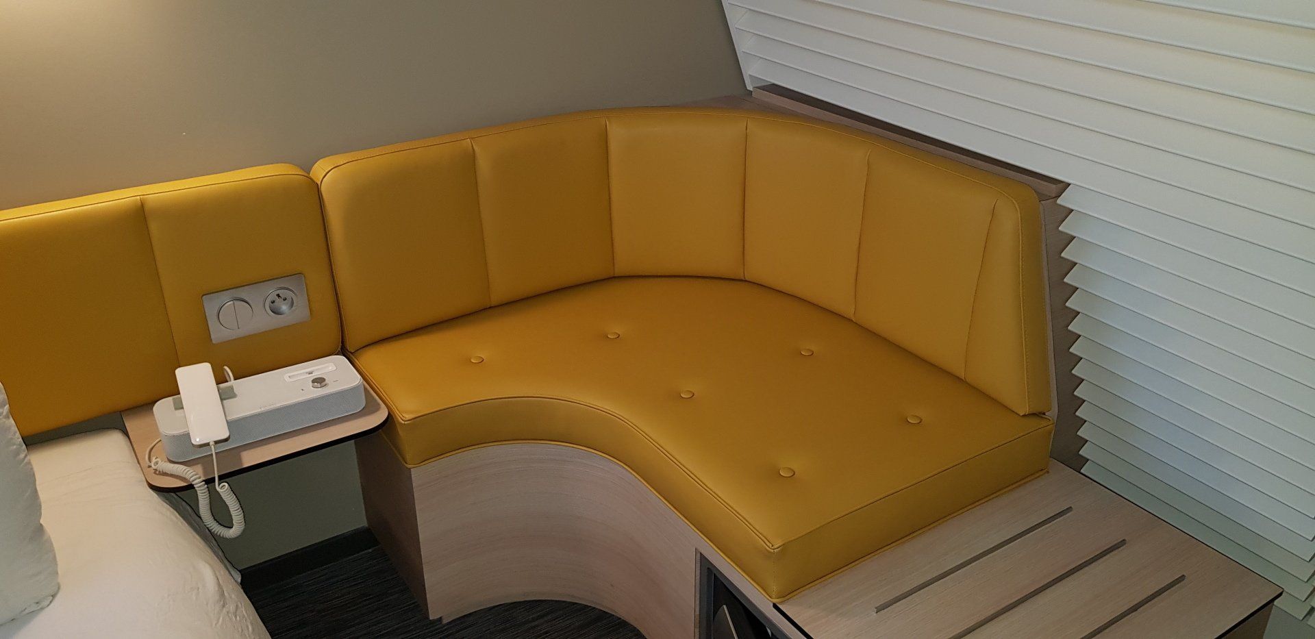 Cabine jaune courbée dans une pièce, avec une table intégrée et un téléphone.