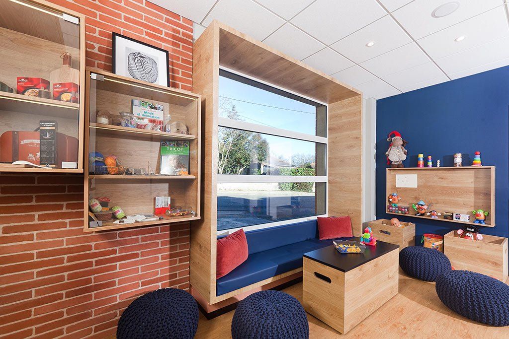 Salle de jeux avec un siège de fenêtre intégré, des jouets sur des étagères et des murs en briques et bleus.