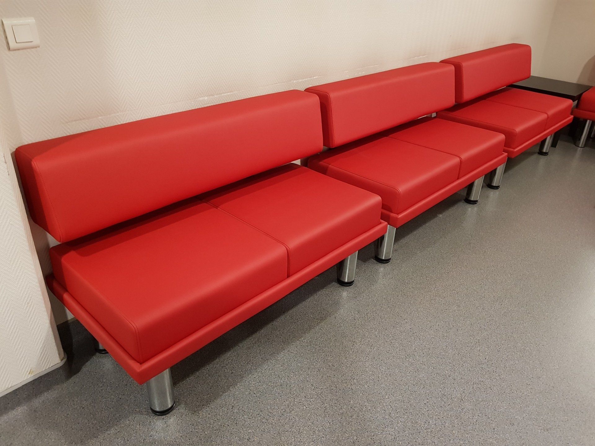 Canapé de salle d'attente modulaire rouge contre un mur beige et un sol gris.