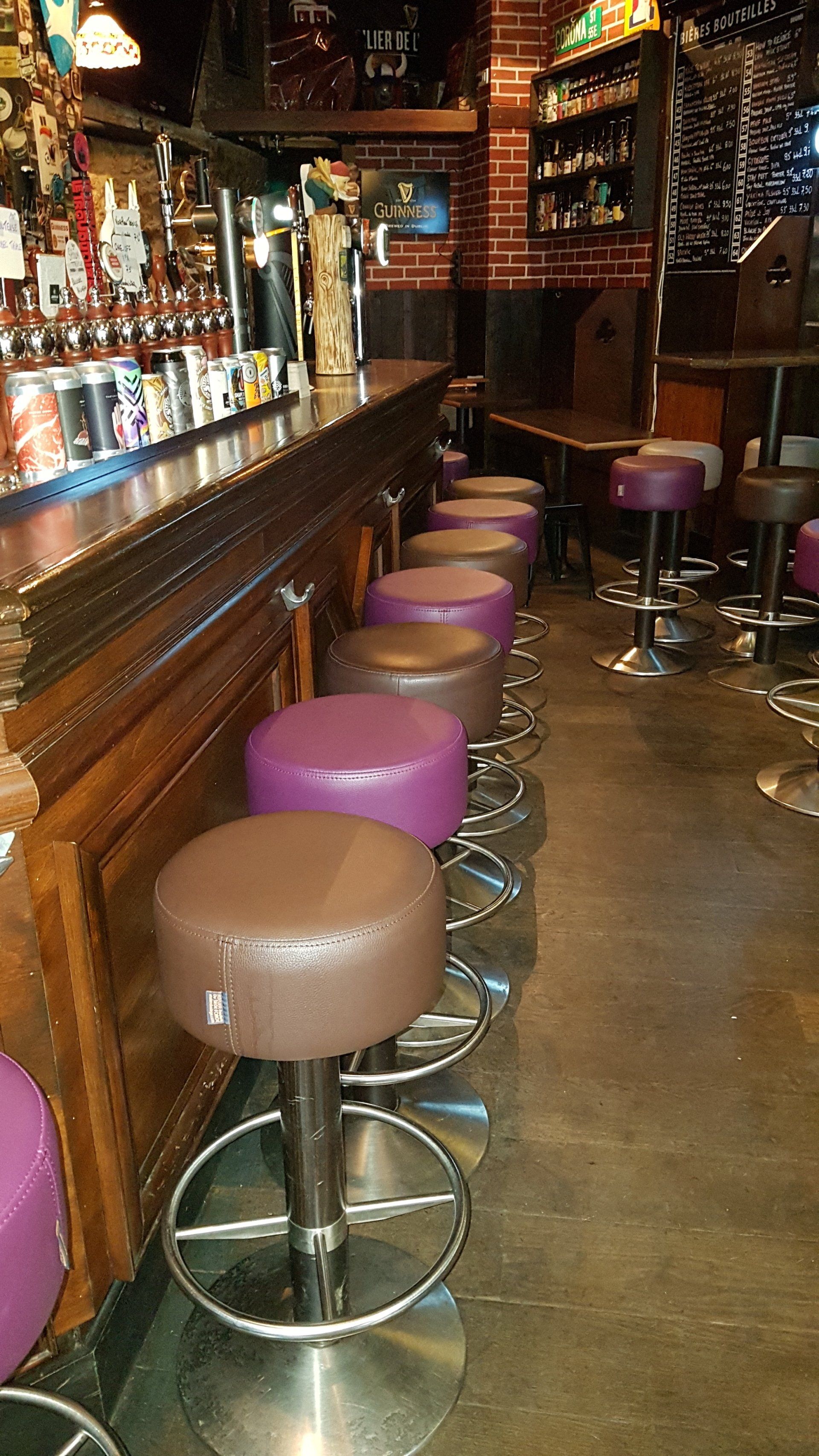 Rangée de tabourets de bar marron et violets alignés devant un bar en bois.