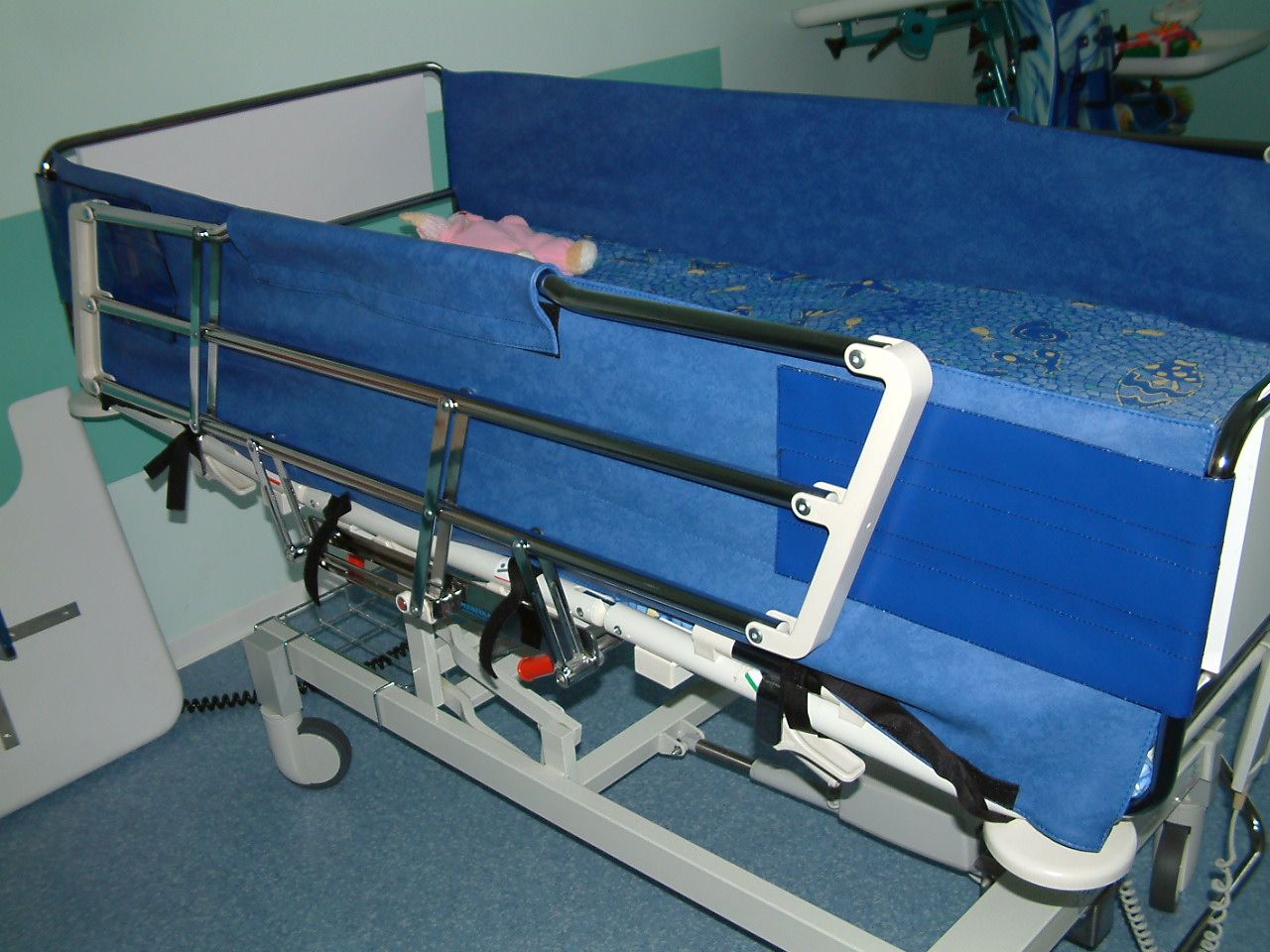 Lit d'hôpital avec rembourrage bleu et barrières de sécurité.