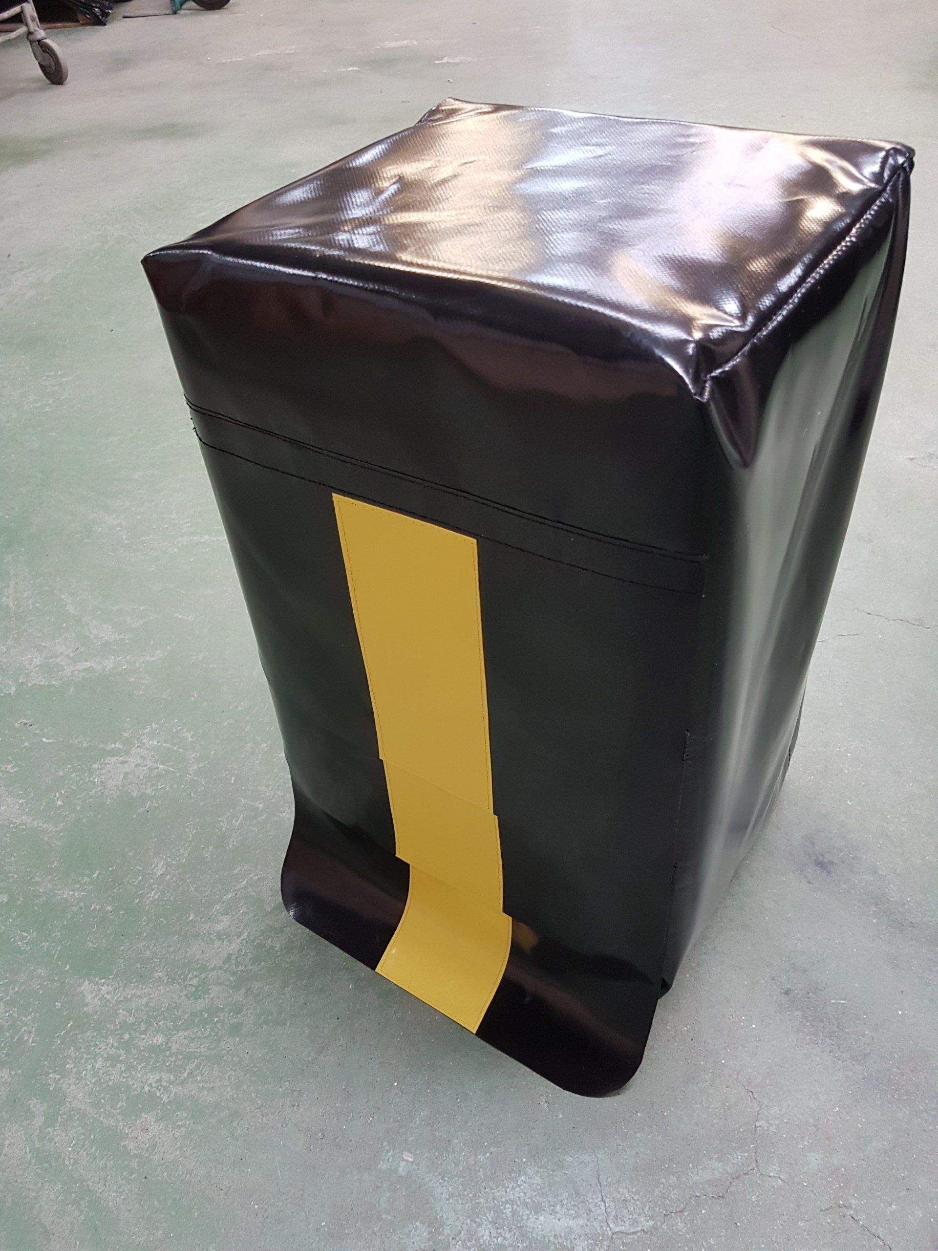 Poteau de sécurité rembourré noir et jaune, de forme rectangulaire, sur une surface grise.