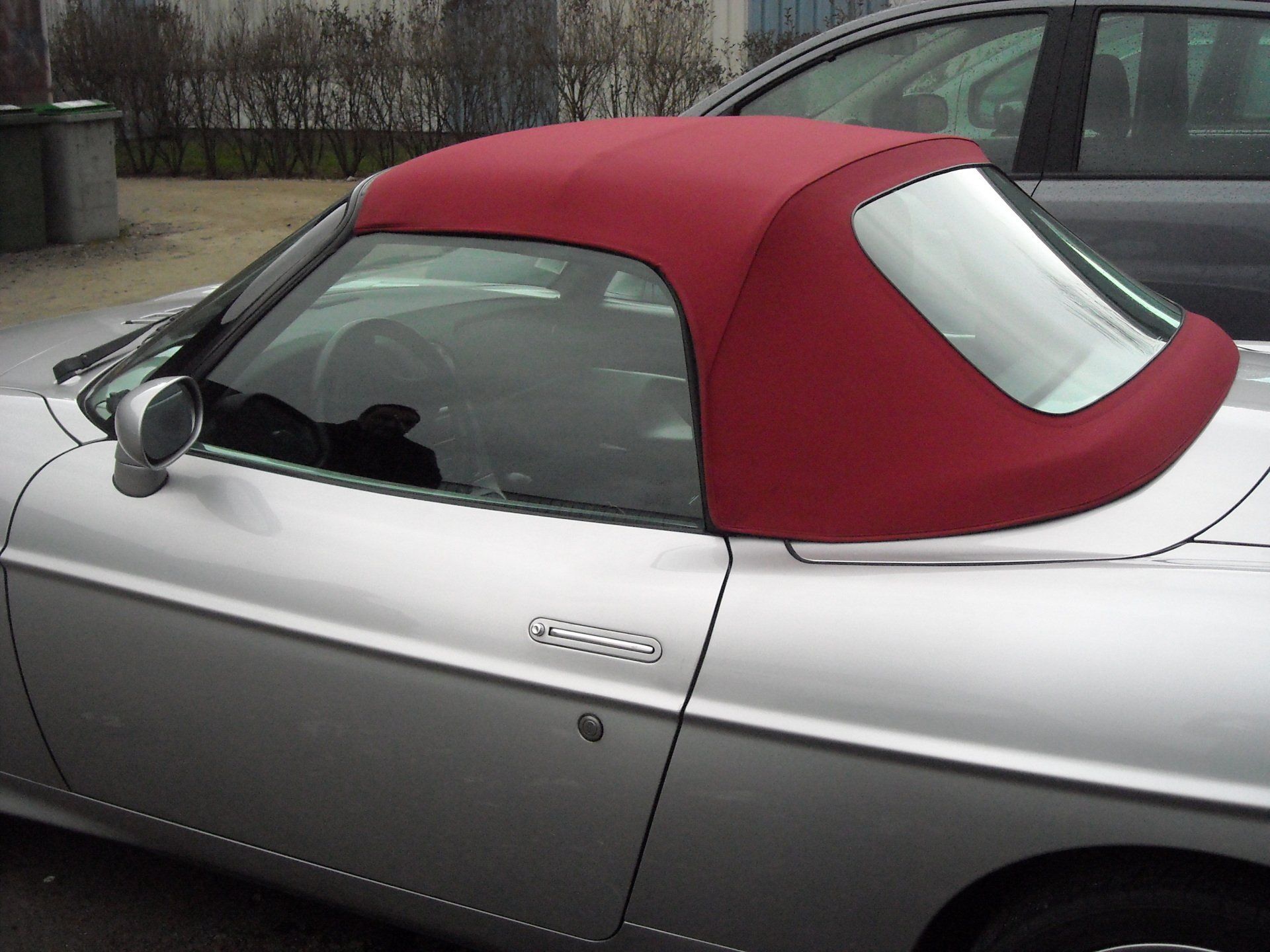 Voiture décapotable argentée avec capote rouge, garée à l'extérieur.