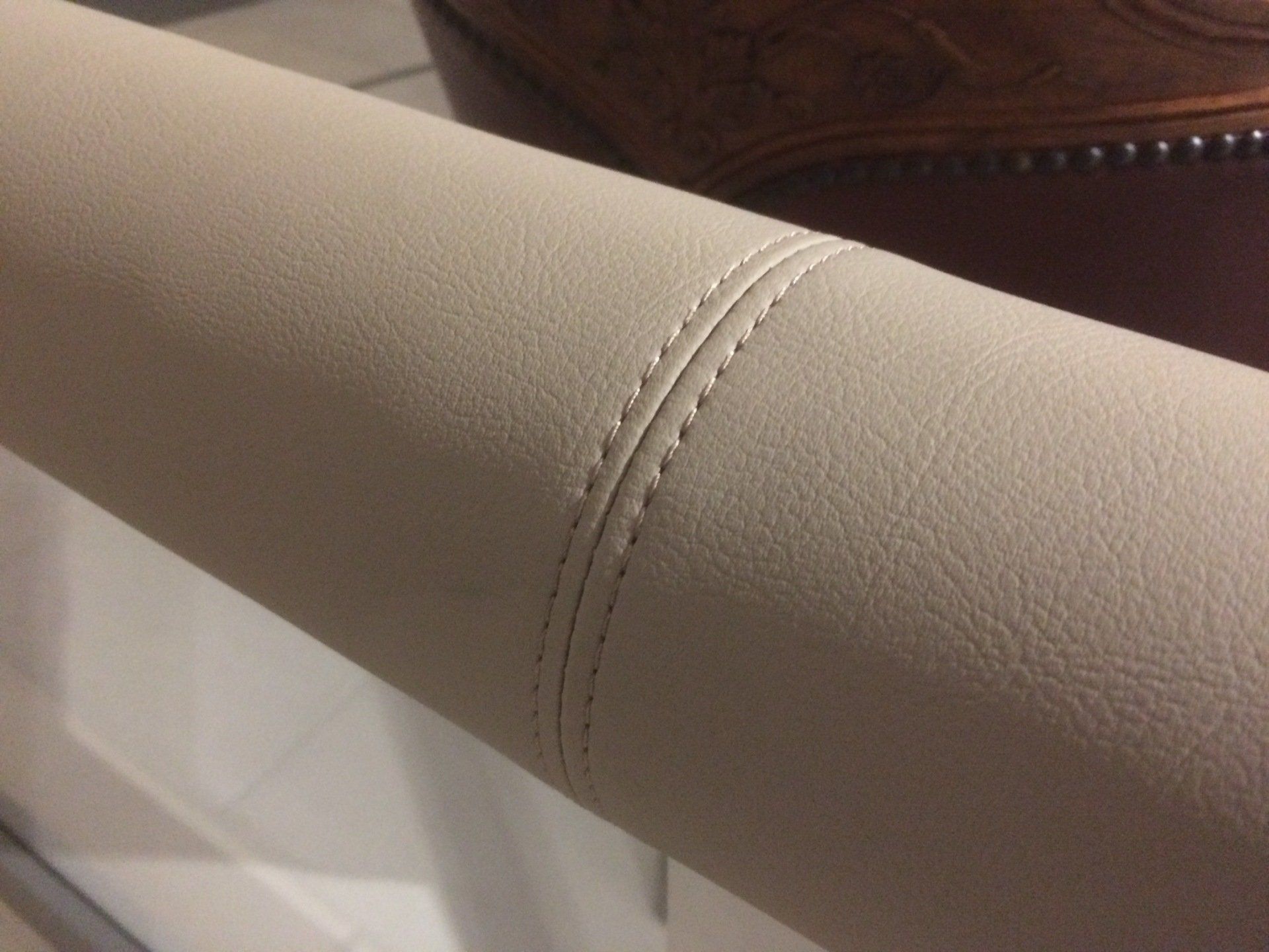 Gros plan d'un accoudoir en cuir beige avec double couture.