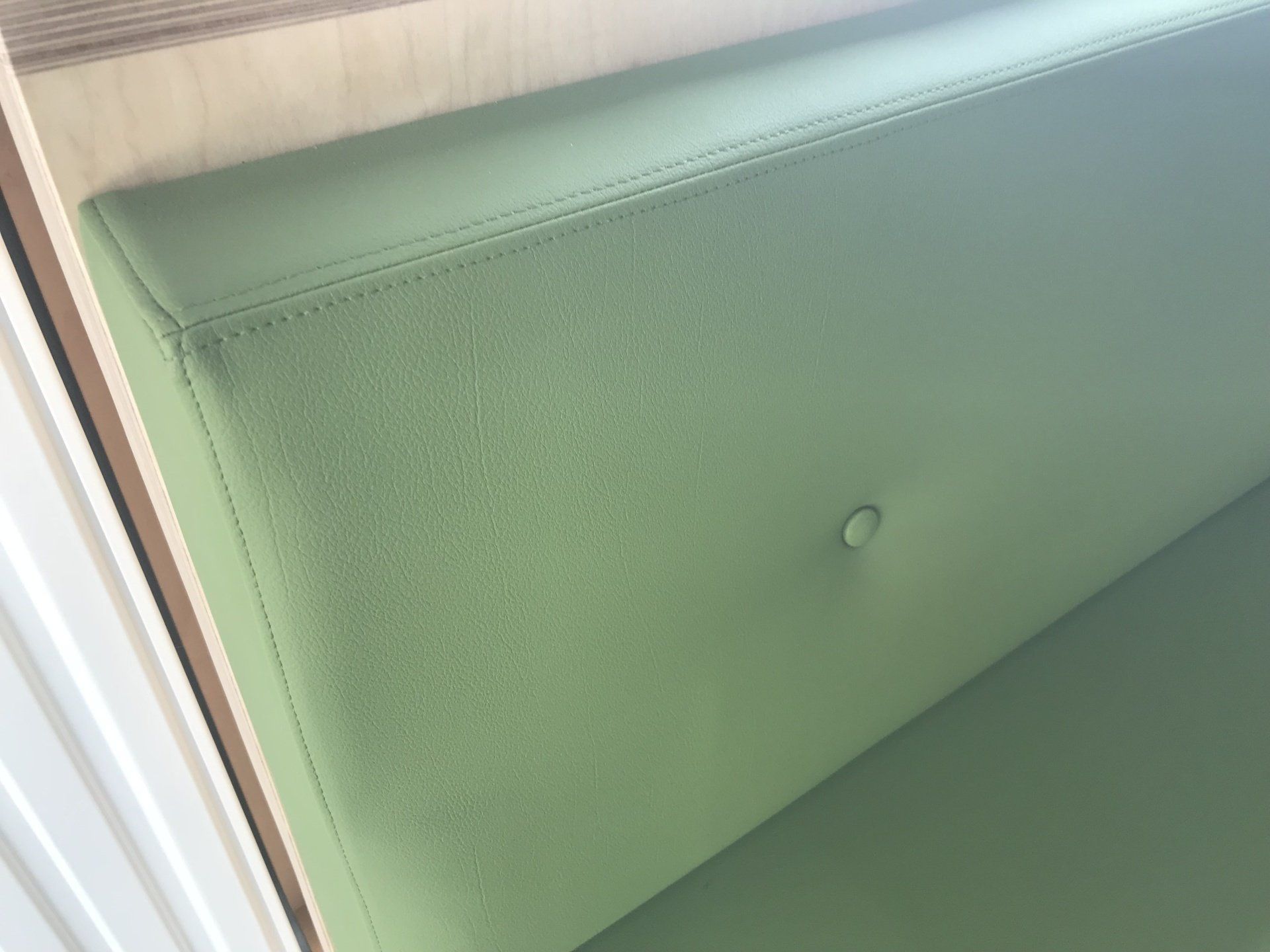 Cabine rembourrée verte avec détails de boutons, placée dans un cadre en bois de couleur claire.