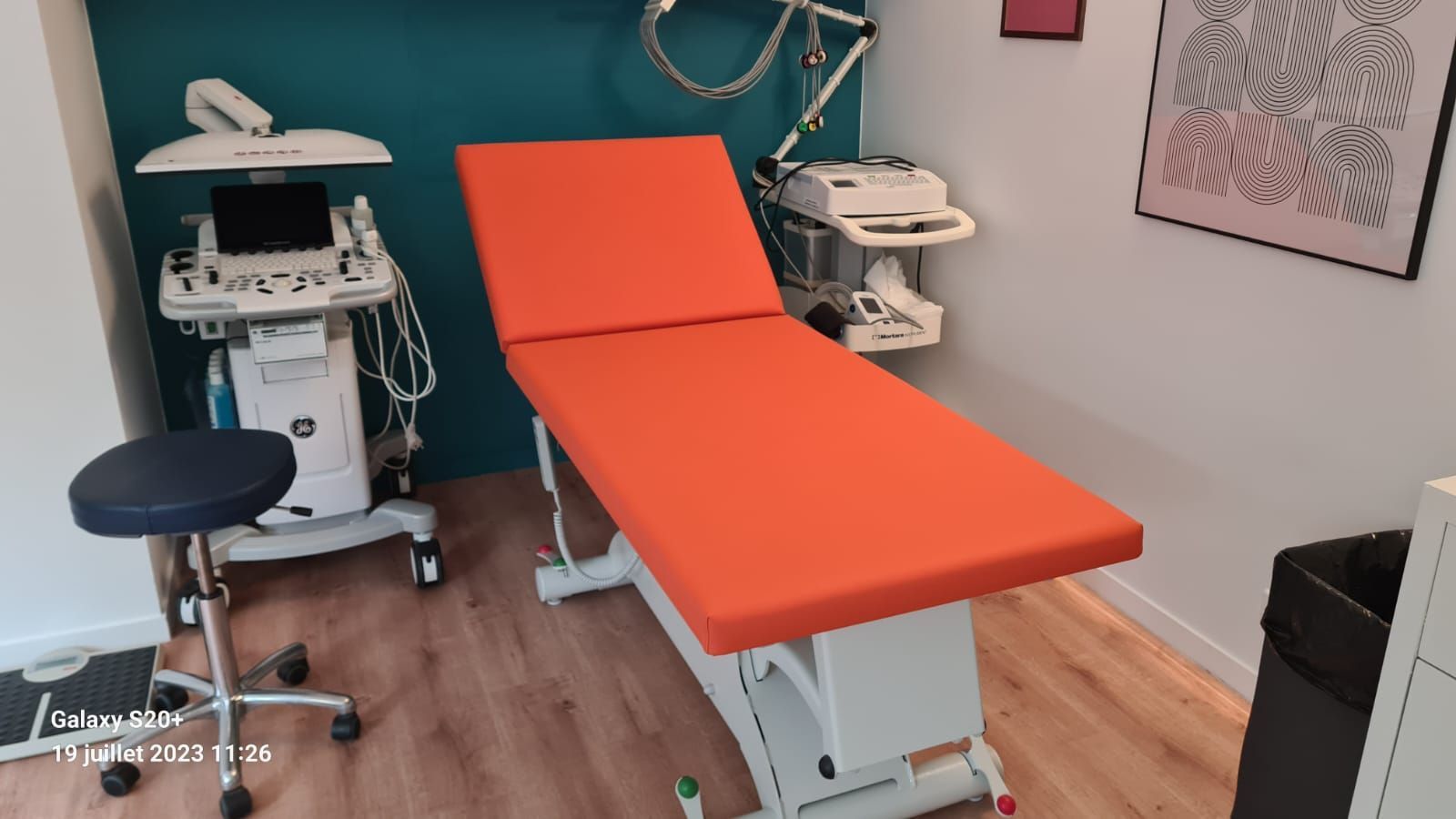 Salle d'examen avec table médicale orange, échographe et tabouret.