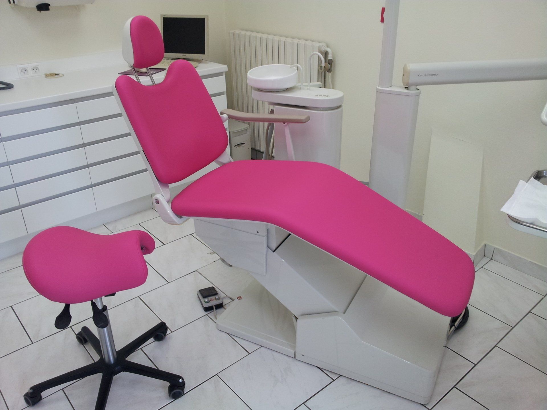 Chaise et tabouret dentaires roses dans le cabinet d'un dentiste avec d'autres équipements en arrière-plan.