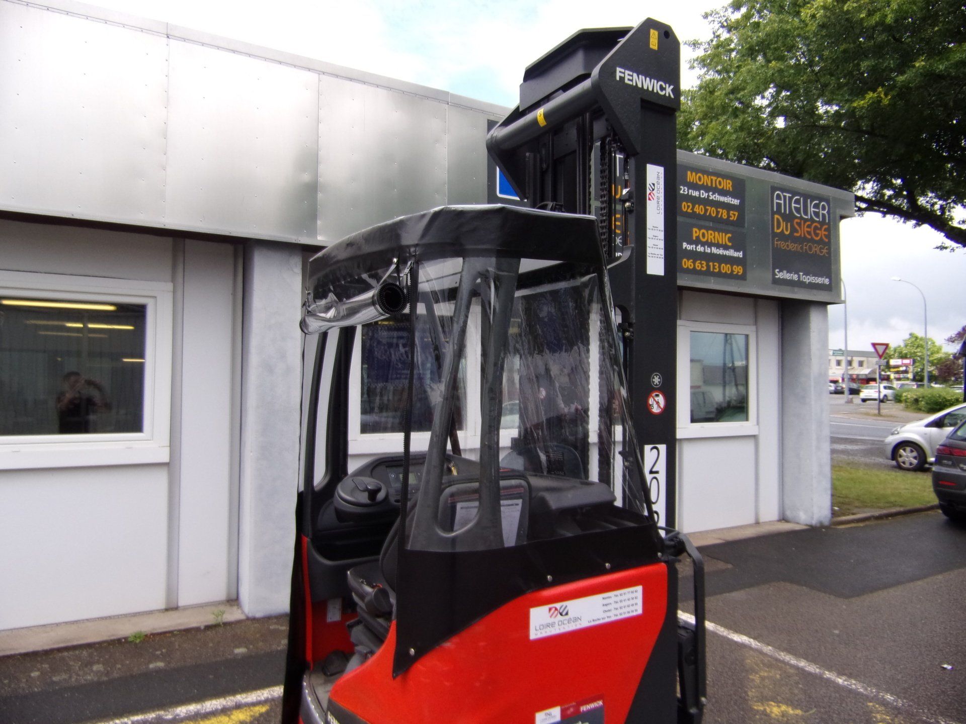 Chariot élévateur rouge et noir stationné à l'extérieur d'un bâtiment avec signalisation.