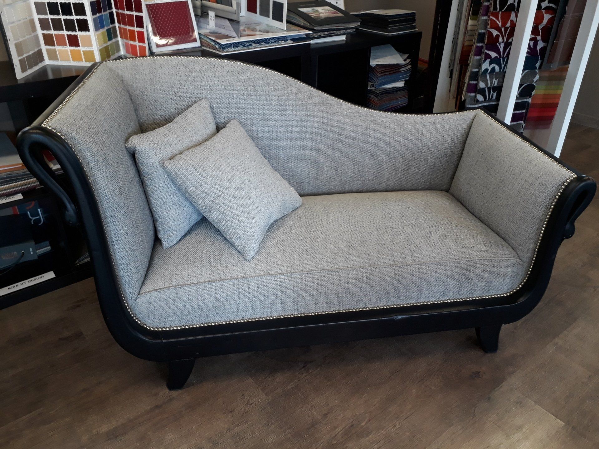 Chaise longue rembourrée grise avec bordure noire et deux oreillers.