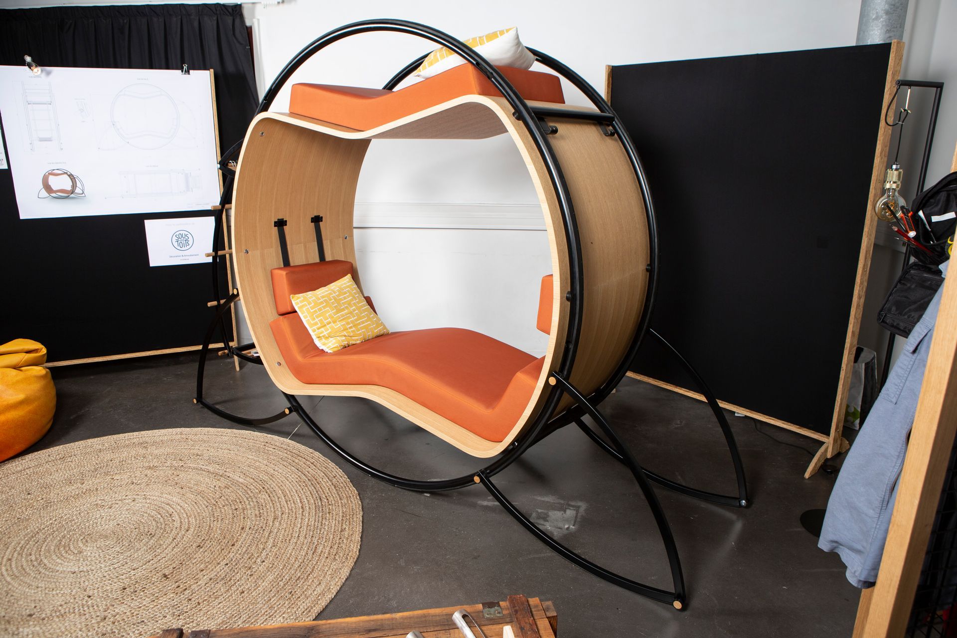 Une chaise longue d'intérieur circulaire unique avec des coussins orange, sur un tapis circulaire dans une pièce.