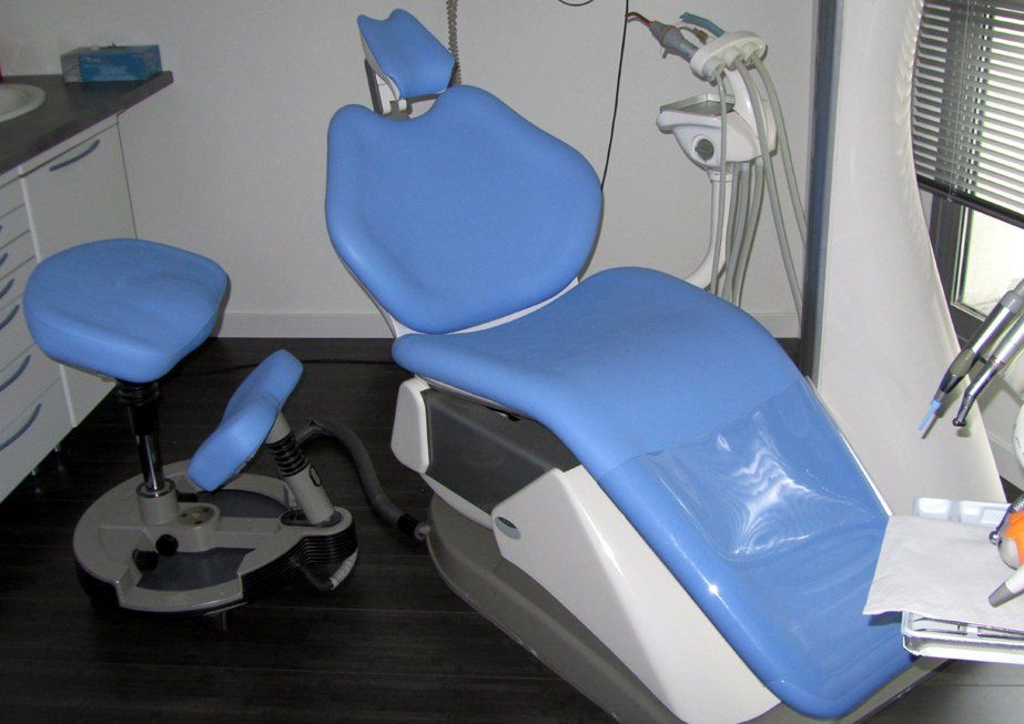 Chaise et tabouret dentaires bleus dans un cabinet dentaire ; instruments visibles en arrière-plan.