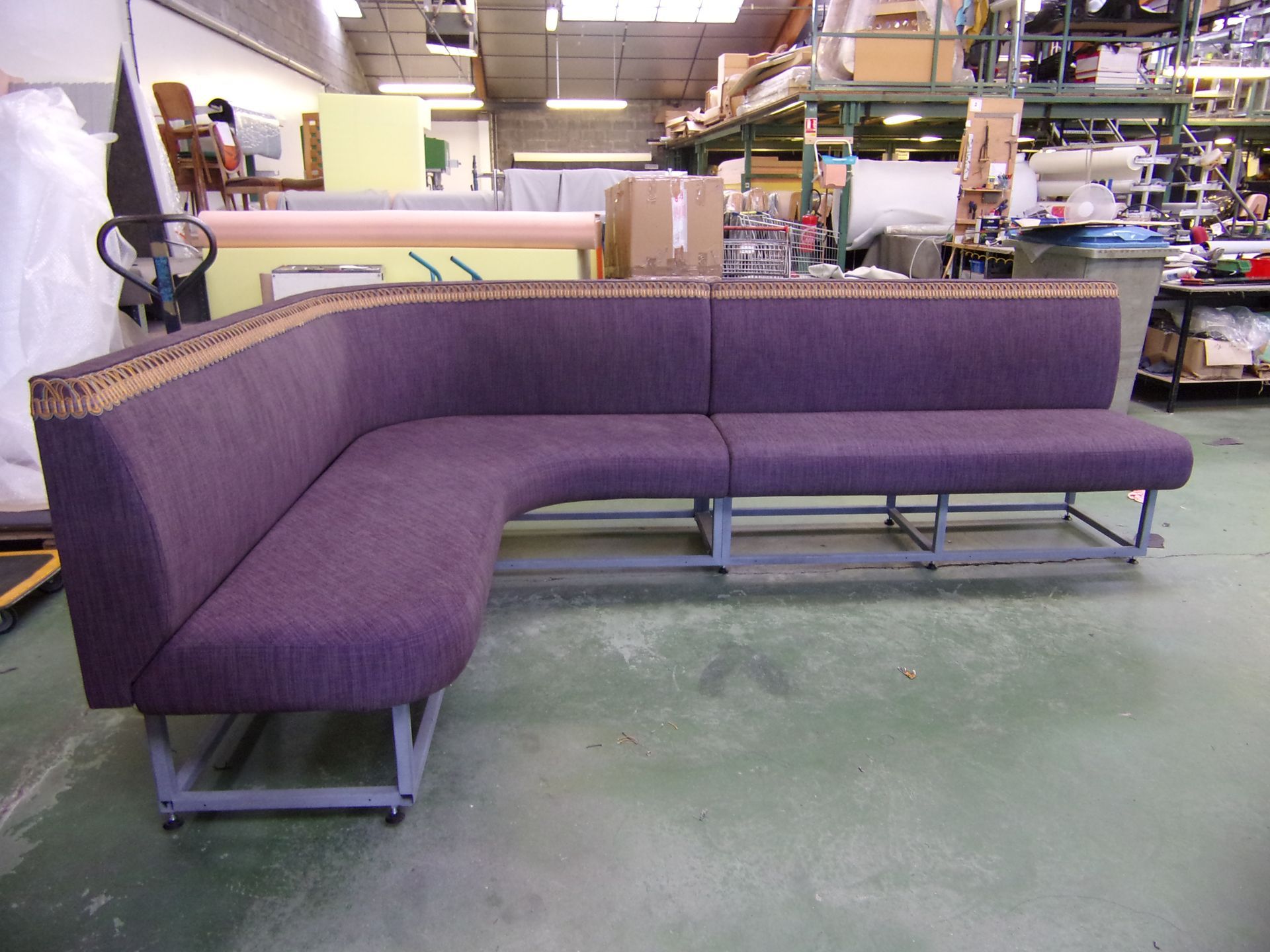 Canapé sectionnel rembourré en forme de L violet avec bordure dorée dans un entrepôt.