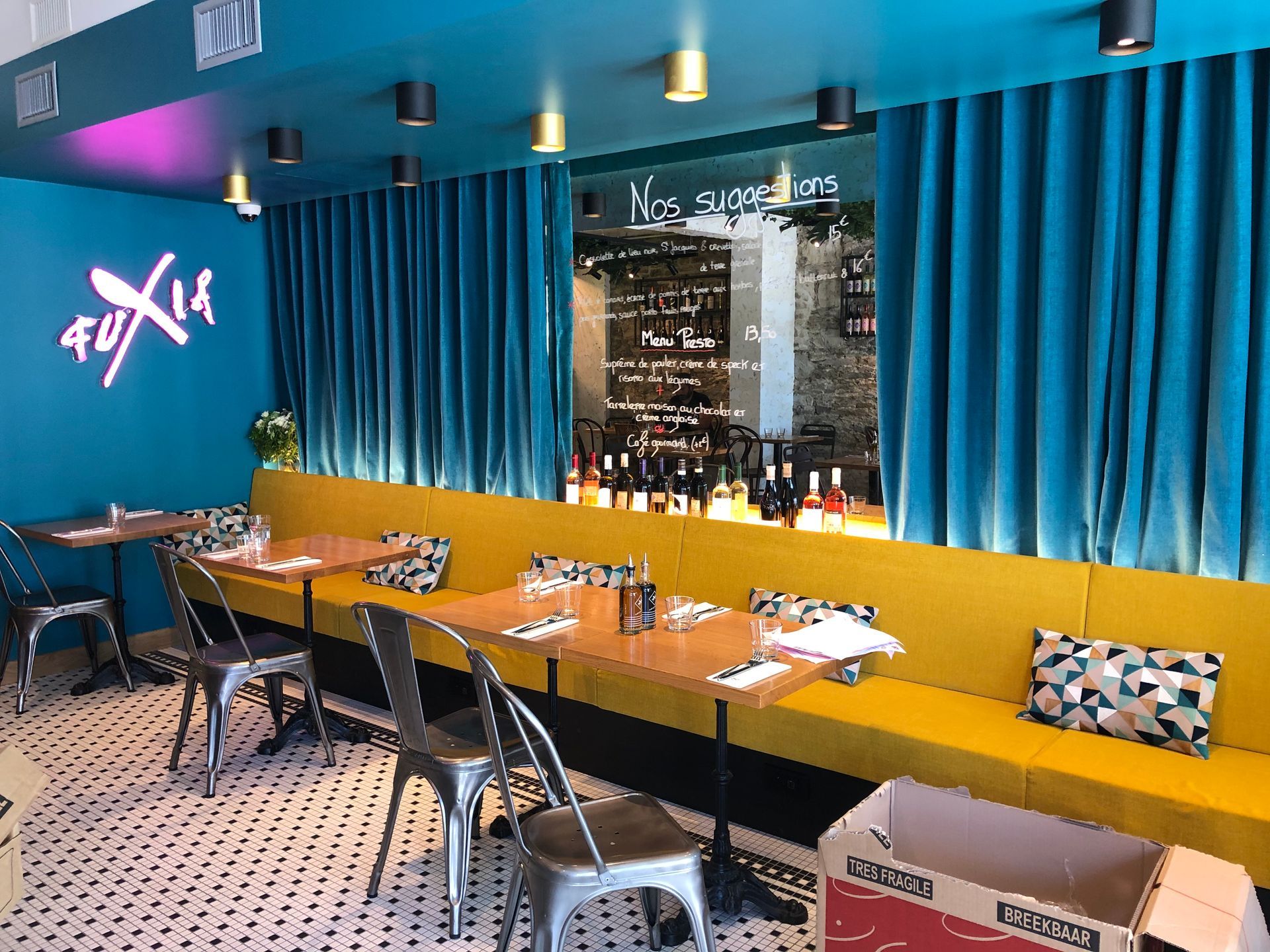 Intérieur de restaurant avec murs et rideaux bleu sarcelle, sièges de cabine jaunes et chaises en métal.