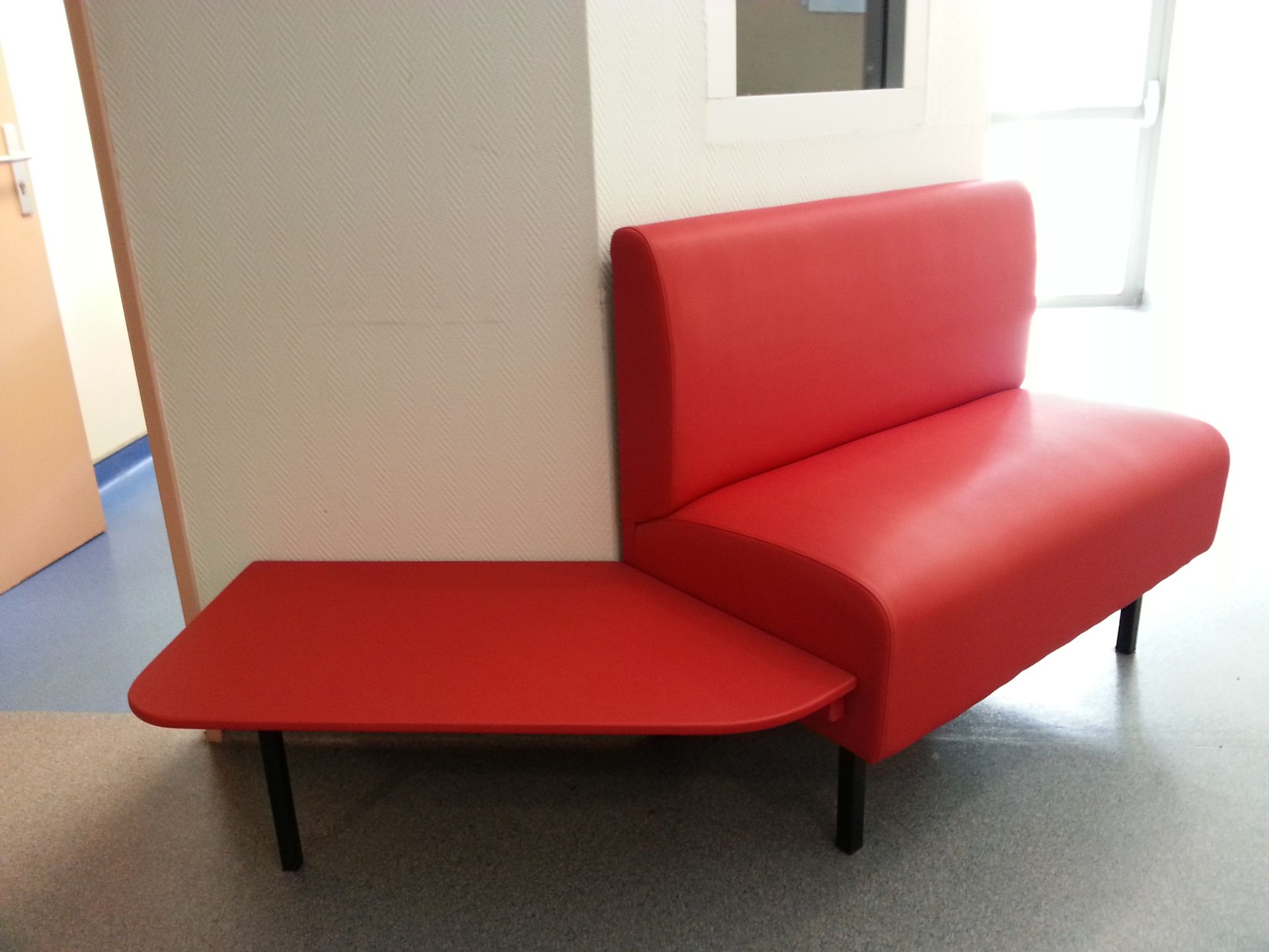 Banc rouge avec table attenante, dans un couloir de couleur claire.