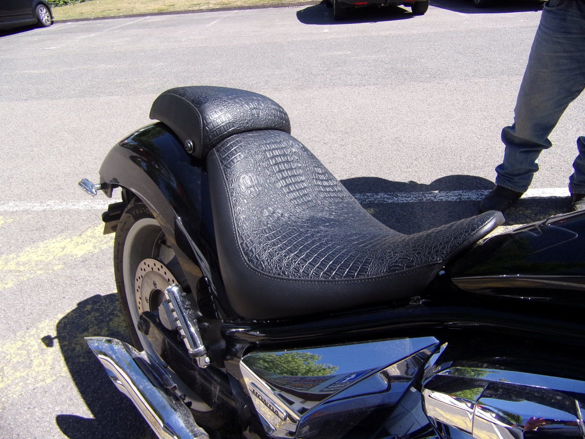 Selle de moto noire avec dossier, en extérieur à la lumière du jour.