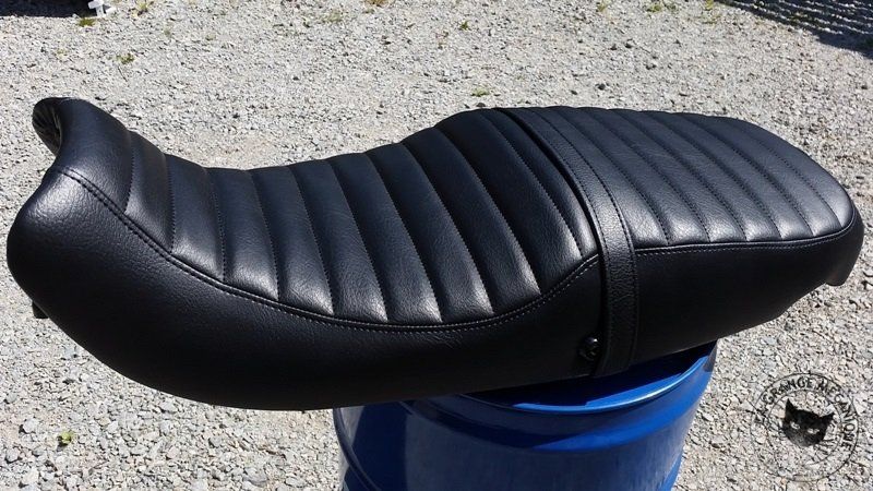 Selle de moto noire à plis cousus sur un tambour bleu.