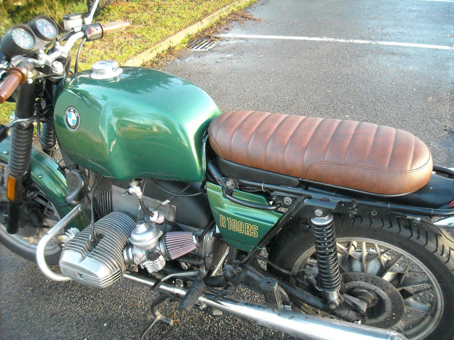 Moto BMW R100 verte avec selle en cuir marron, garée à l'extérieur.