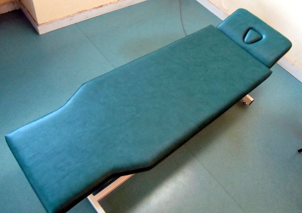 Table de massage verte sur un sol bleu sarcelle dans un cadre médical.