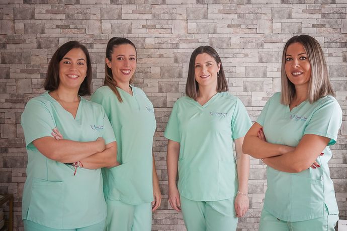 Cuatro mujeres vestidas con uniforme médico posan para una fotografía frente a una pared de ladrillos.