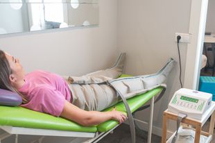 Una mujer está acostada en una cama verde recibiendo un masaje en las piernas.