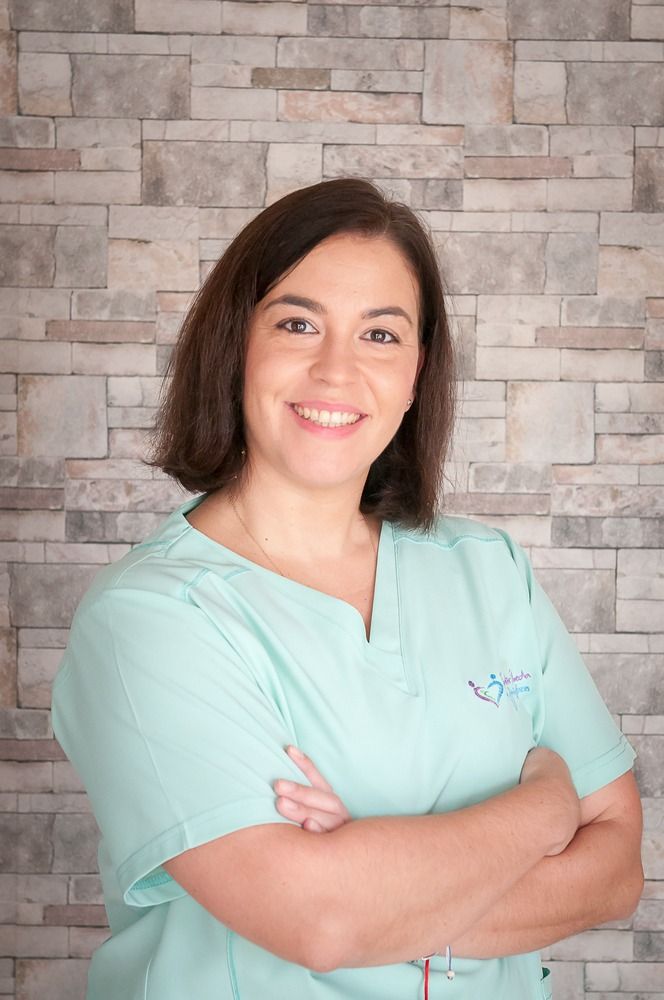 Una mujer con un uniforme médico posa para una fotografía con los brazos cruzados frente a una pared de ladrillos.
