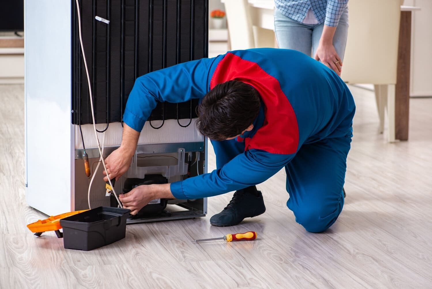 Un hombre está reparando un refrigerador en una cocina.