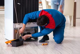 Un hombre está reparando un refrigerador en una cocina.