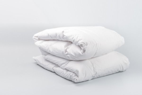 Dos edredones blancos doblados apilados sobre un fondo gris claro.