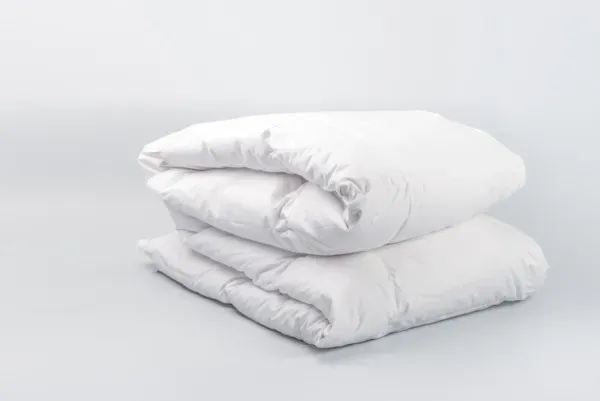Dos edredones blancos doblados apilados sobre un fondo gris claro.