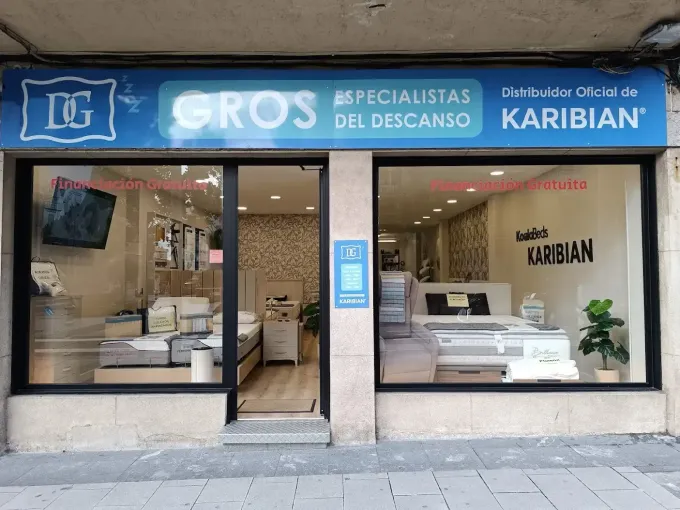 Fachada de una tienda de colchones con letrero azul y escaparates en la acera.