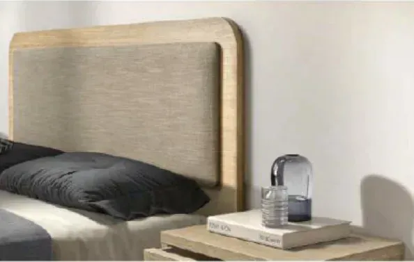 Mesita de noche con lámpara y libro junto a una cama con almohada negra y cabecero tapizado en color beige.
