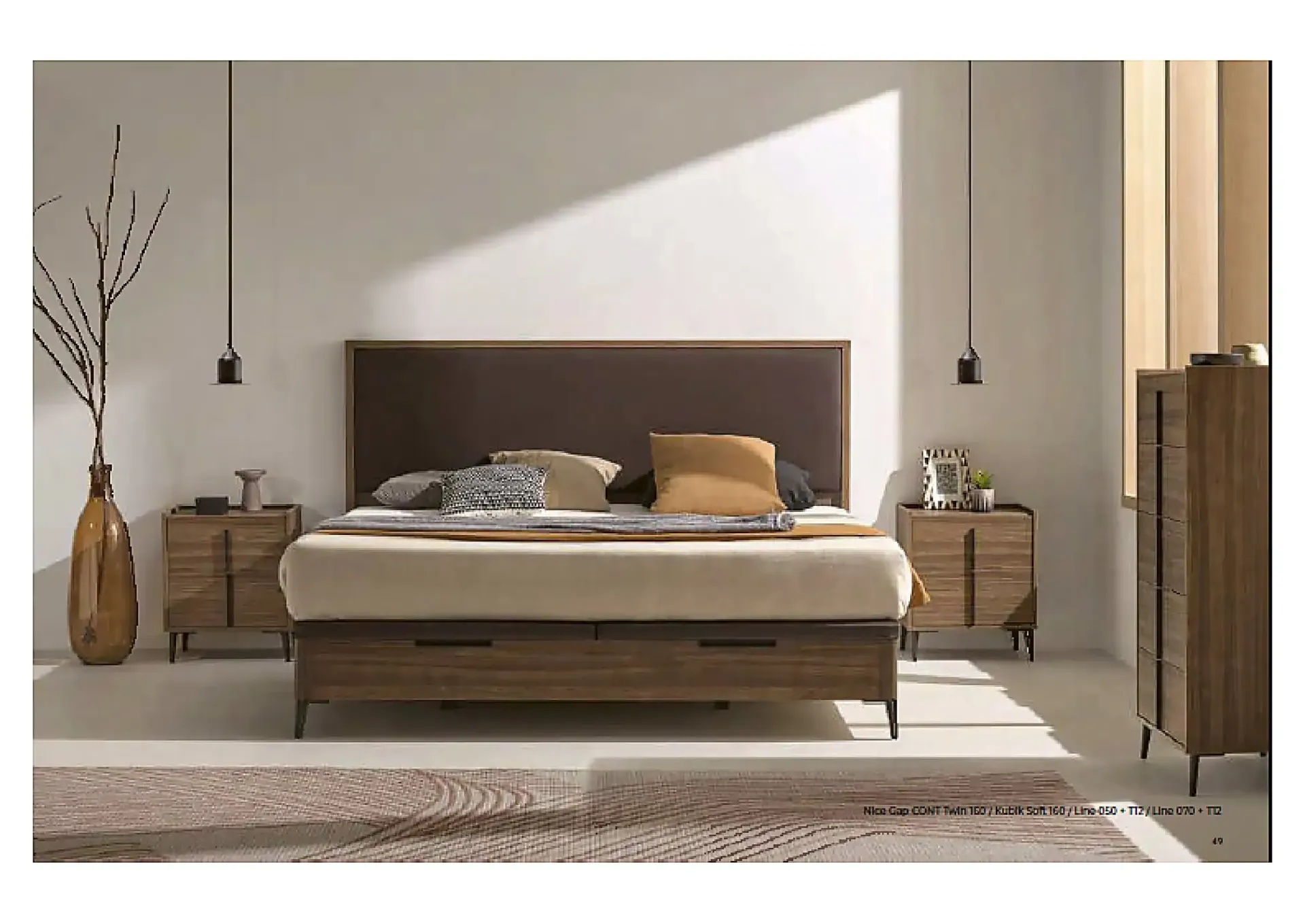 Dormitorio moderno con cama tapizada en gris, colchón blanco, almohadas negras y una manta oscura.