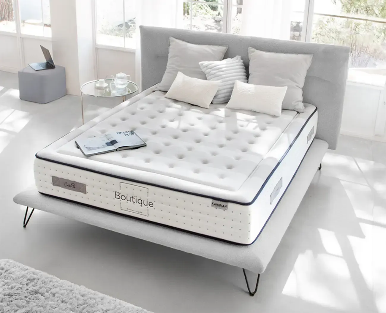 Dormitorio moderno con cama tapizada en gris, colchón blanco, almohadas negras y una manta oscura.