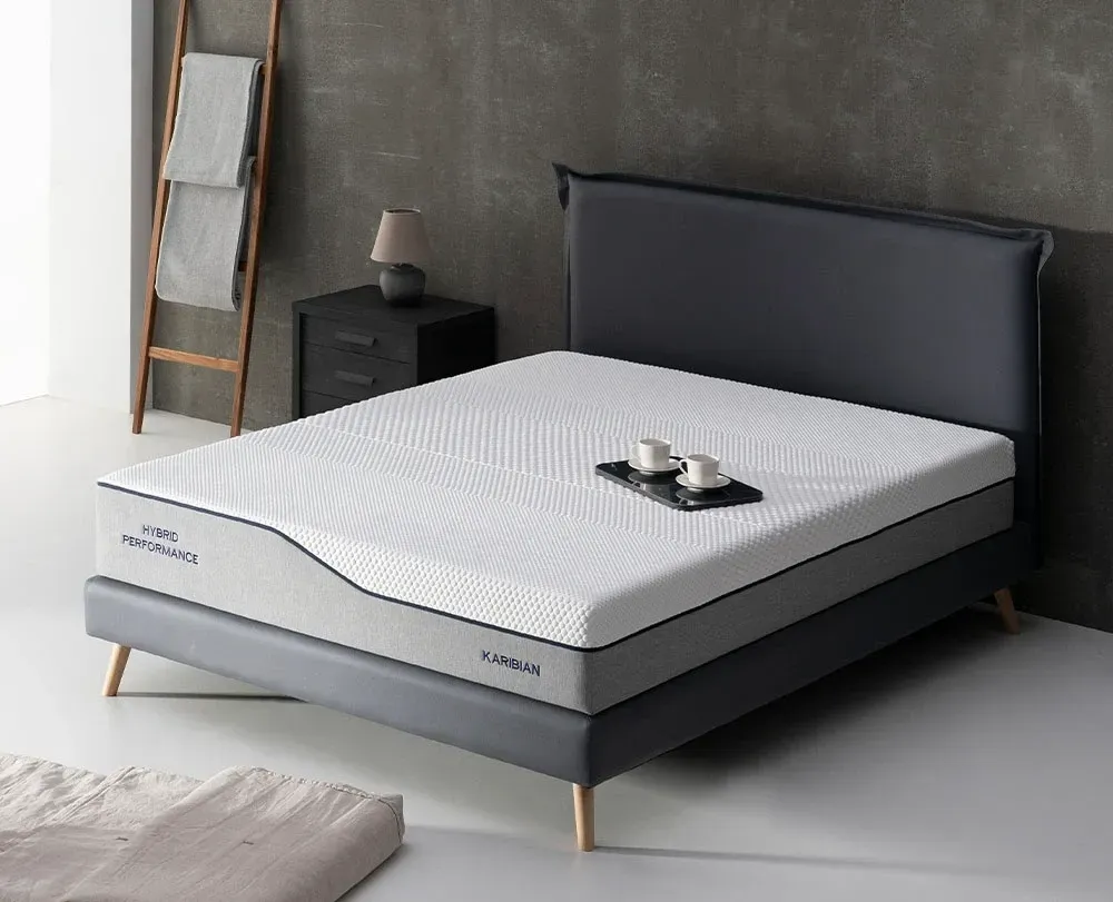 Dormitorio moderno con cama tapizada en gris, colchón blanco, almohadas negras y una manta oscura.