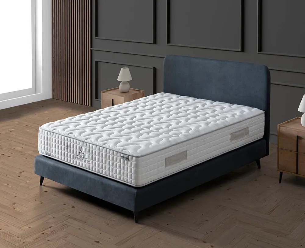 Cama tapizada en azul con colchón acolchado blanco en un dormitorio moderno.
