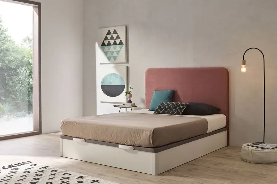 Dormitorio minimalista con cabecero rosa, cama beige, lámpara de pie y ventana grande.