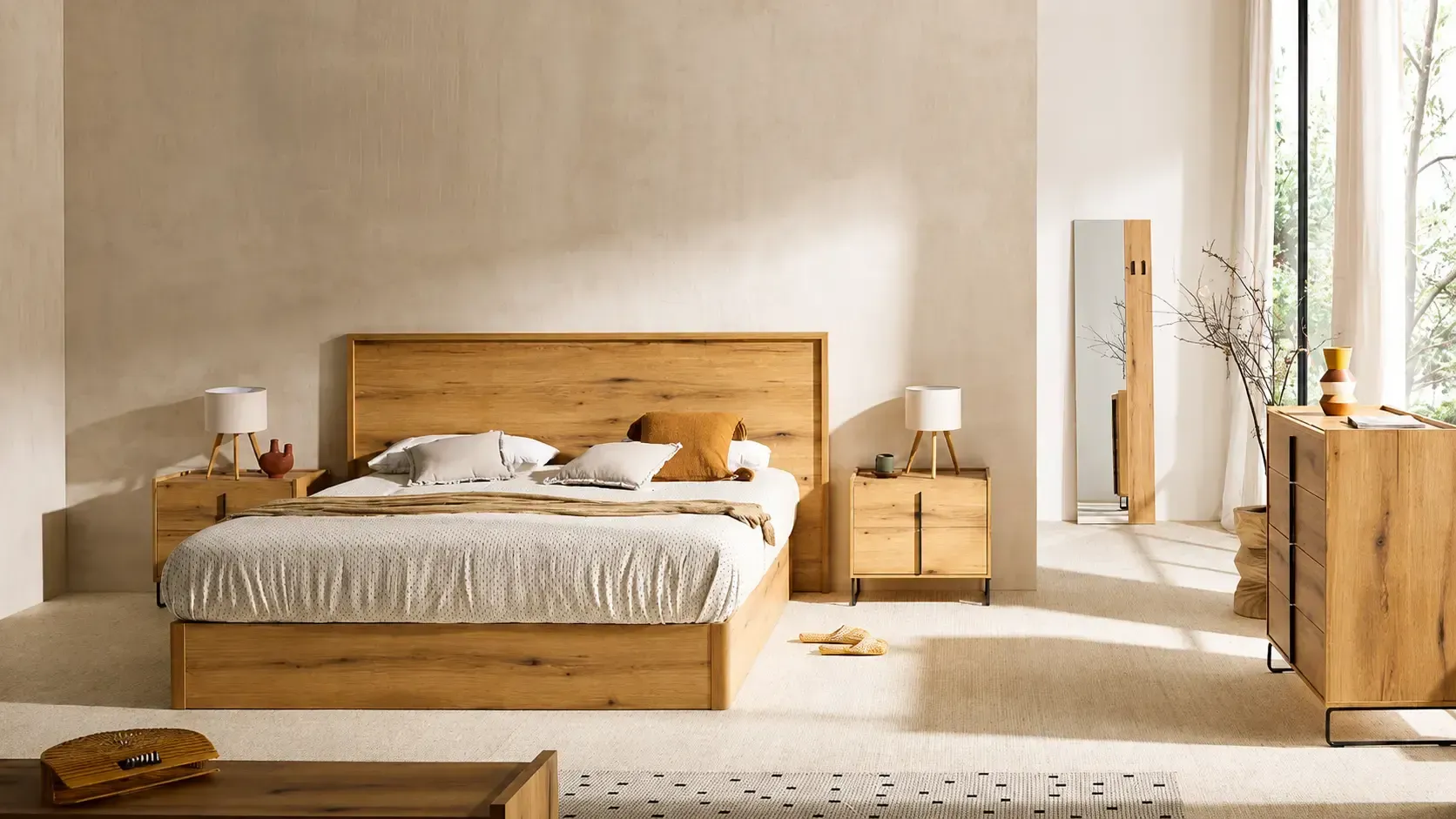 Dormitorio moderno con cama tapizada en gris, colchón blanco, almohadas negras y una manta oscura.