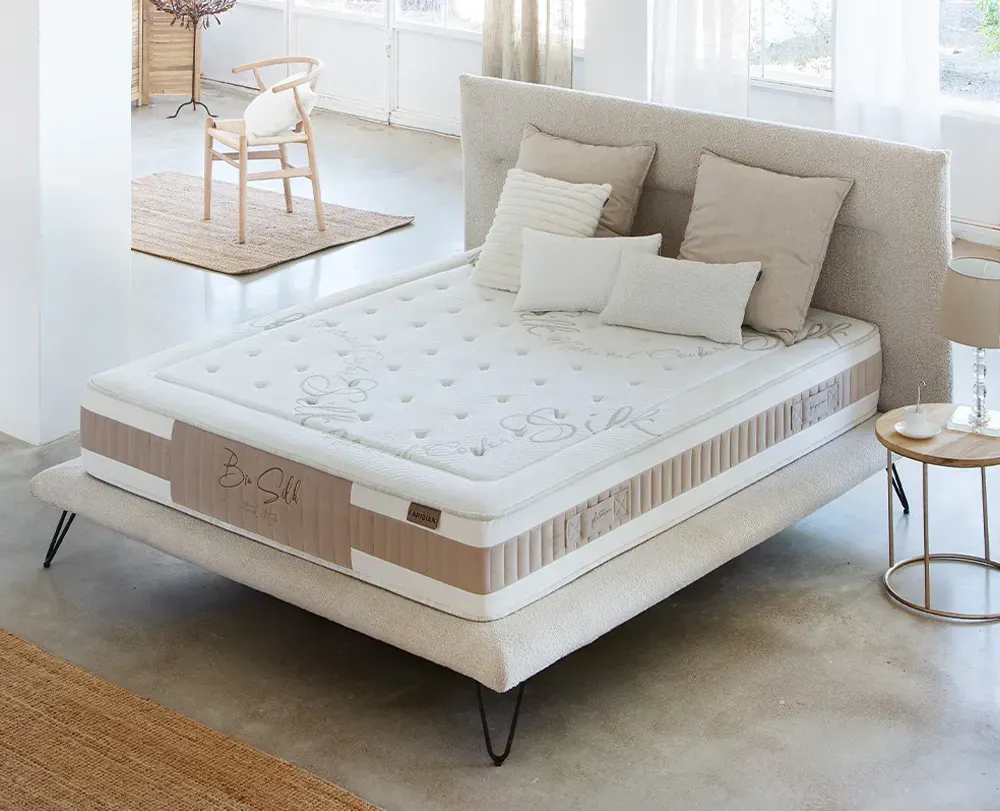 Dormitorio moderno con cama tapizada en gris, colchón blanco, almohadas negras y una manta oscura.