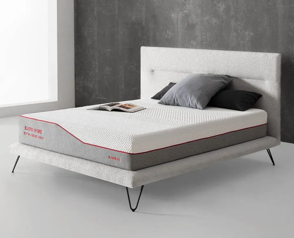 Cama tapizada moderna con colchón gris, almohadas y cabecero blanco en un dormitorio minimalista.