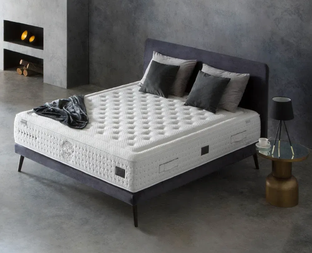 Dormitorio moderno con cama tapizada en gris, colchón blanco, almohadas negras y una manta oscura.