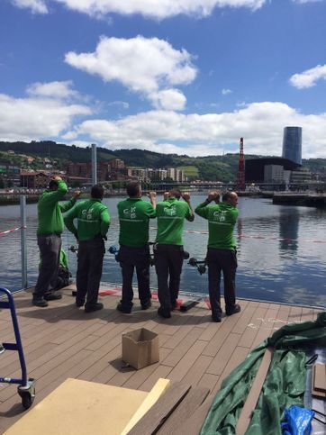 Un grupo de hombres con camisas verdes están parados en un muelle con vista a un cuerpo de agua.