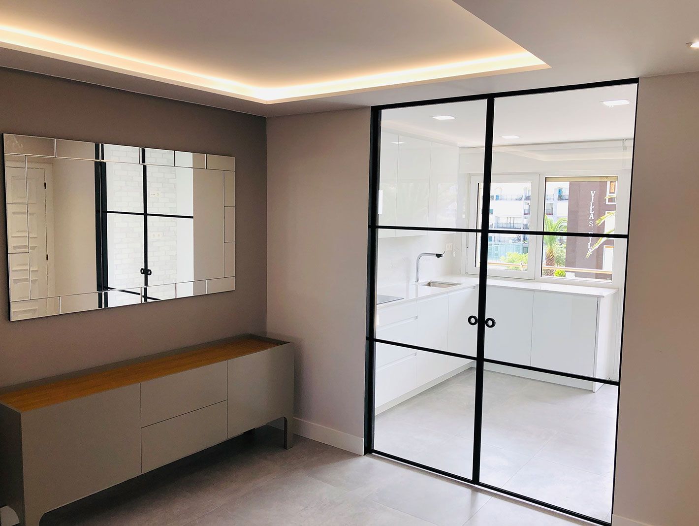 Una habitación con espejo y puertas corredizas de vidrio que conducen a una cocina.