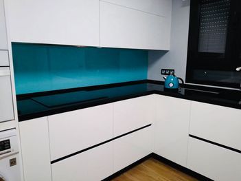 Una cocina con gabinetes blancos, encimeras negras y protector contra salpicaduras azul.