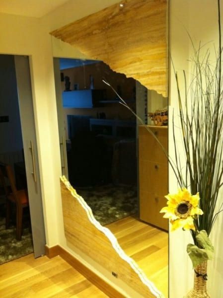 Un espejo roto en un pasillo al lado de un jarrón de flores.