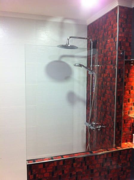 Un baño con azulejos rojos y una ducha con puerta de cristal.